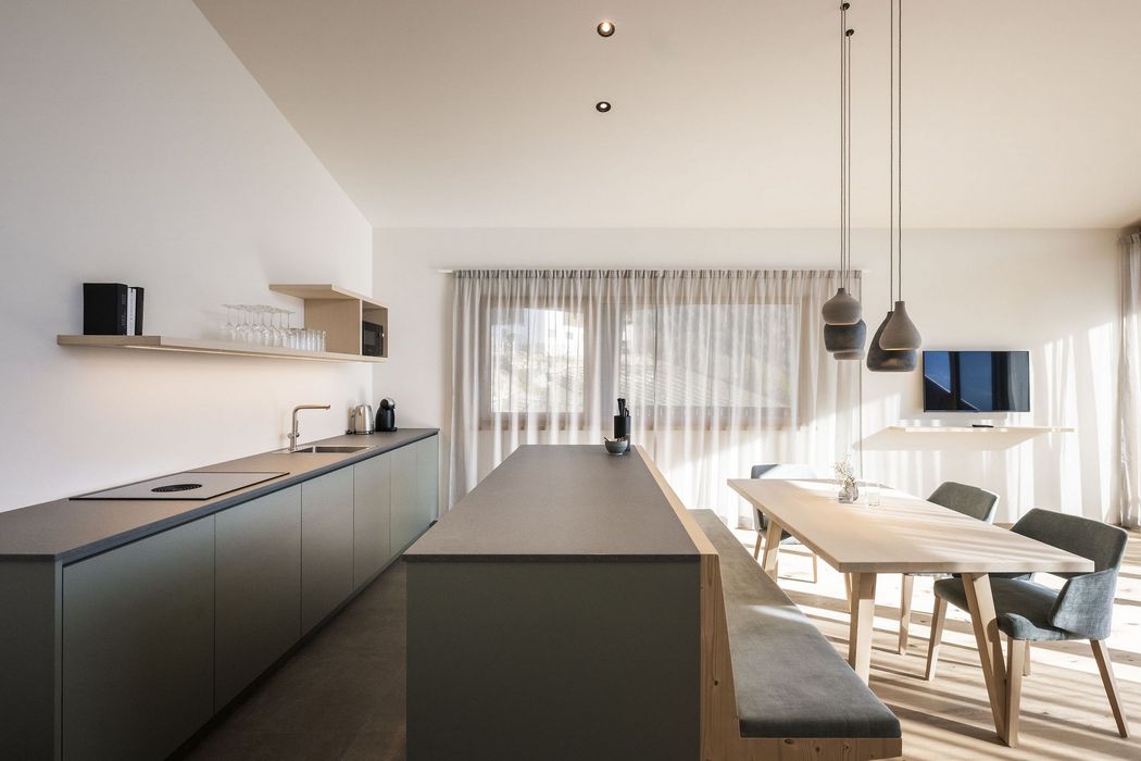 Helle, minimalistische Küche mit langen Arbeitsflächen, offenem Essbereich und großem Fenster mit Vorhängen