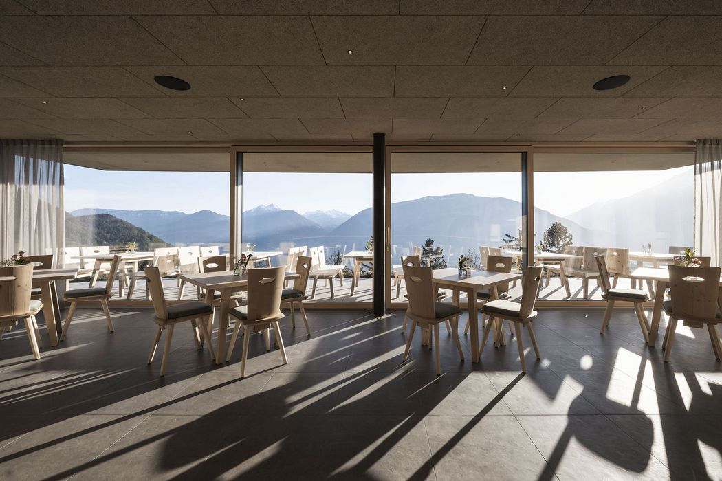 Moderner Innenraum mit Holztischen und Stühlen vor großen Fenstern mit Blick auf Berge bei Sonnenlicht