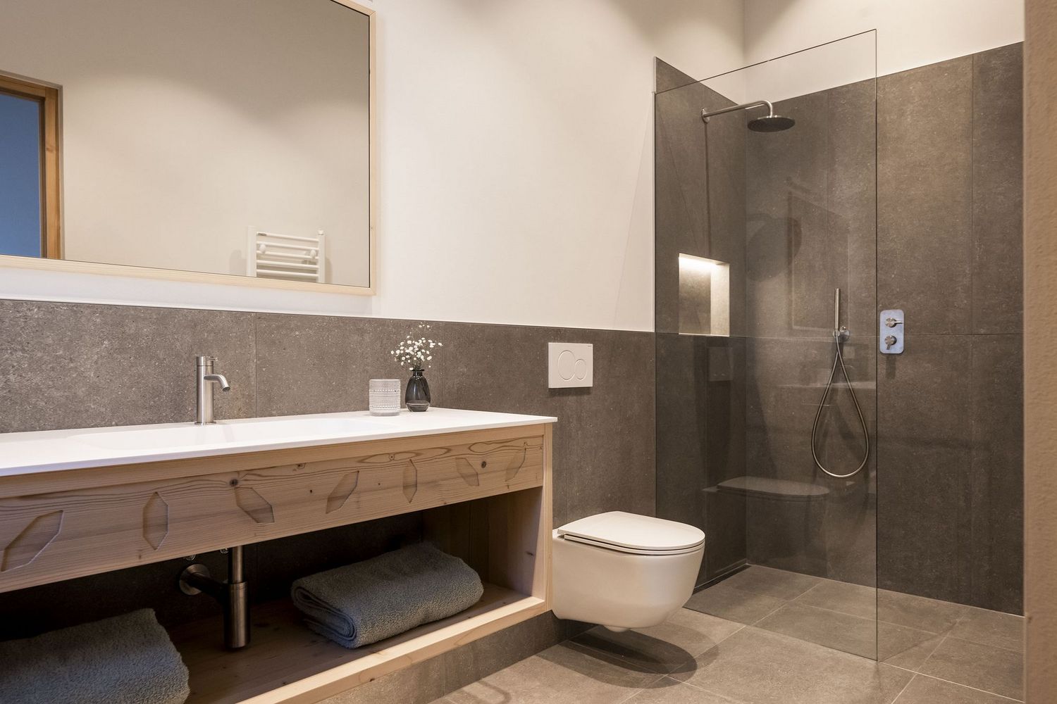 Modernes Badezimmer mit Holzwaschtisch, Wandtoilette und begehbarer Dusche mit Glaswand.