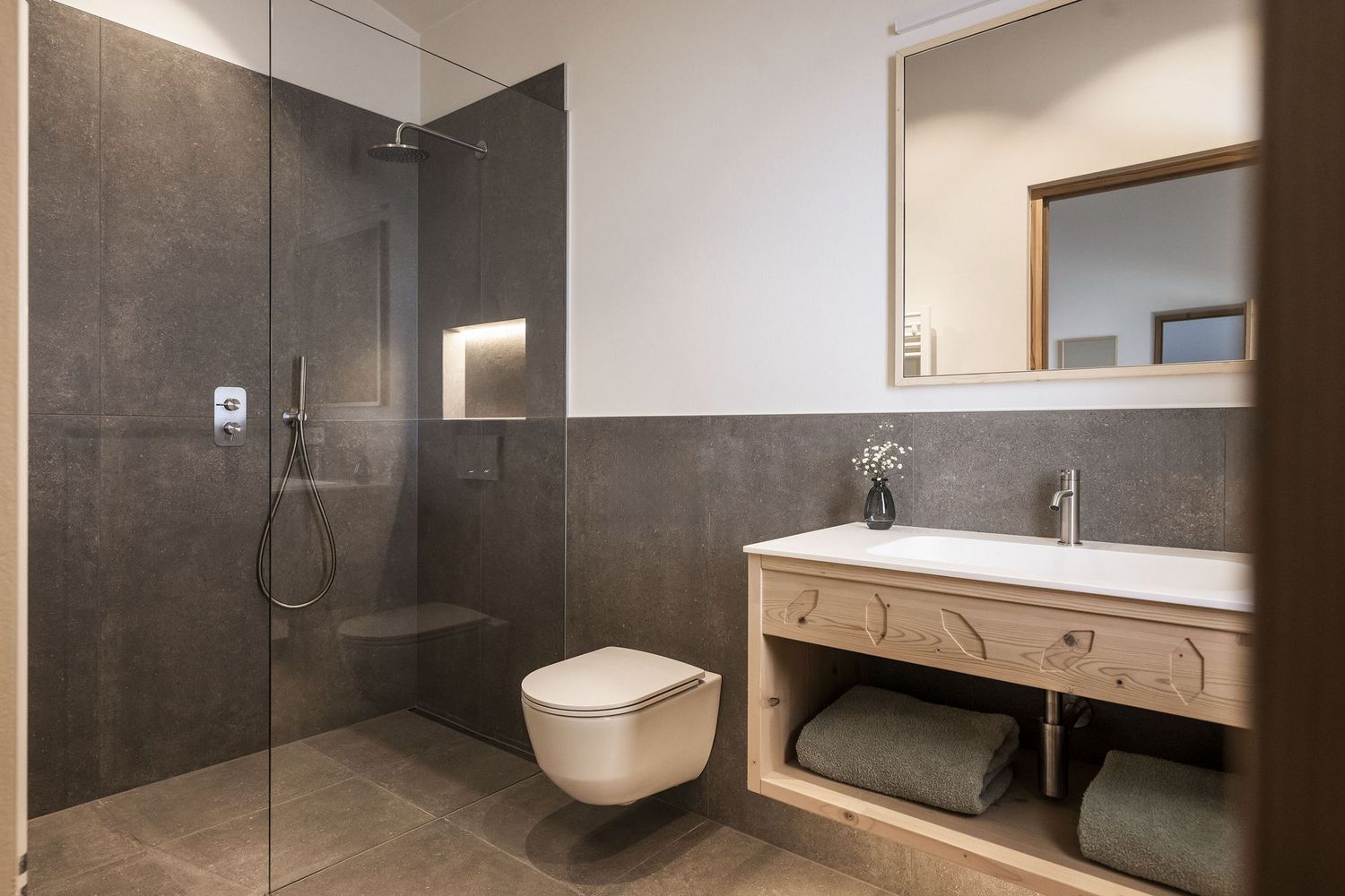 Modernes Badezimmer mit bodengleicher Dusche, hängendem WC, Holzwaschtisch mit Spiegel und grauen Fliesen