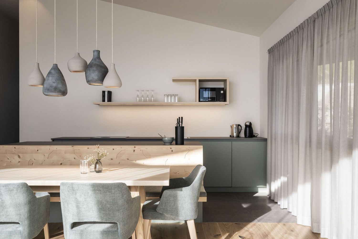 Moderner Essbereich mit Holzbank, grauen Stühlen, Hängelampen und Küchenzeile mit Mikrowelle.