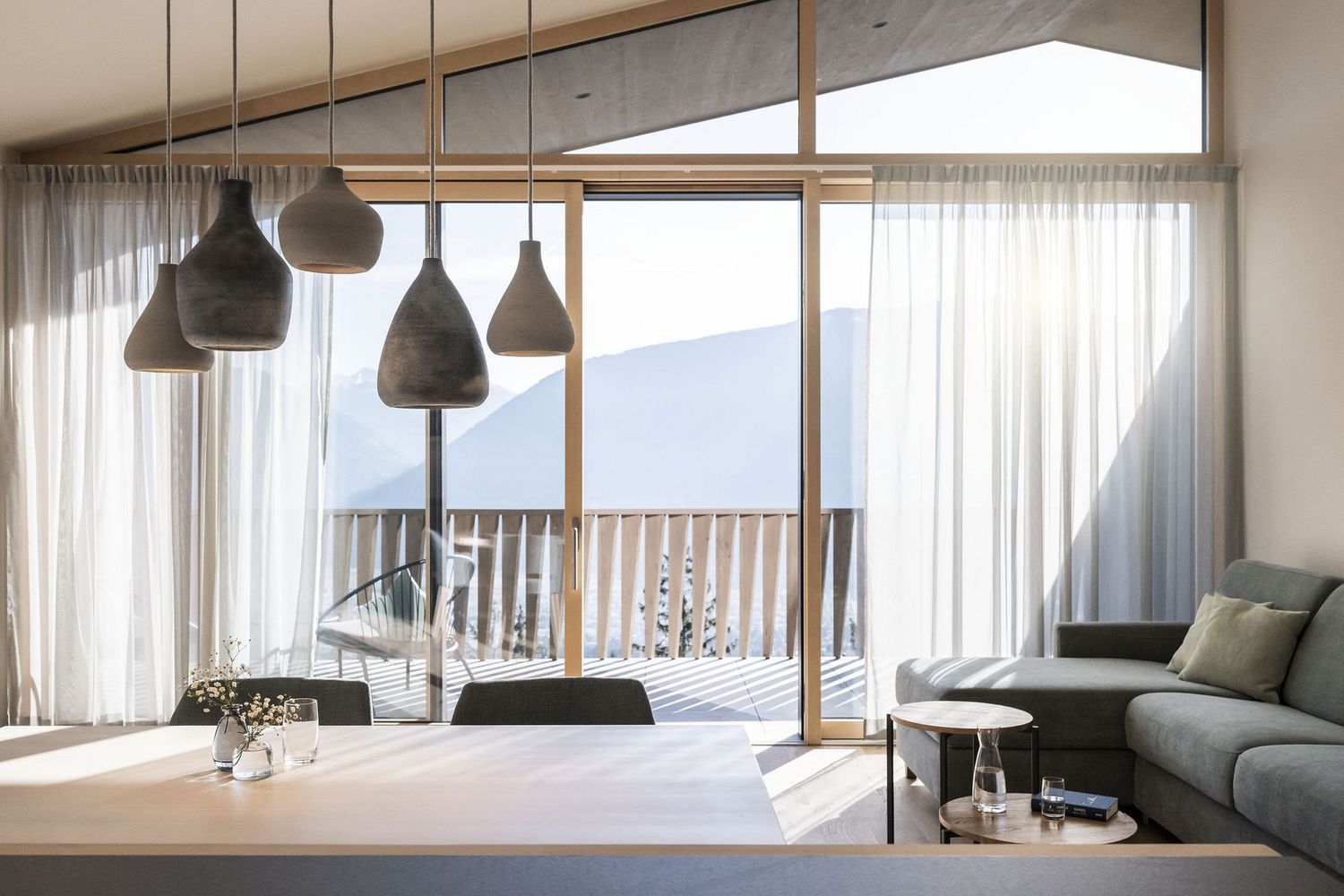 Modernes Wohnzimmer mit grauer Couch, hölzernem Tisch, hängenden Leuchten und großem Fenster mit Bergblick