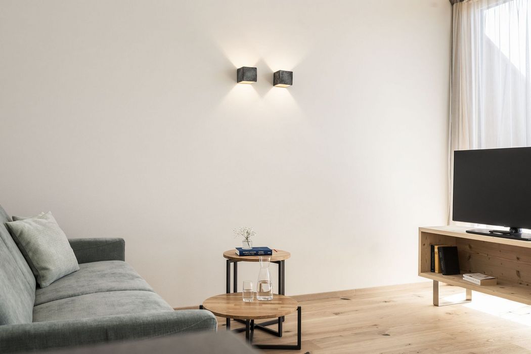 Minimalistisches Wohnzimmer mit grauem Sofa, runden Holztischen, TV auf Holzmöbel und zwei Wandlampen