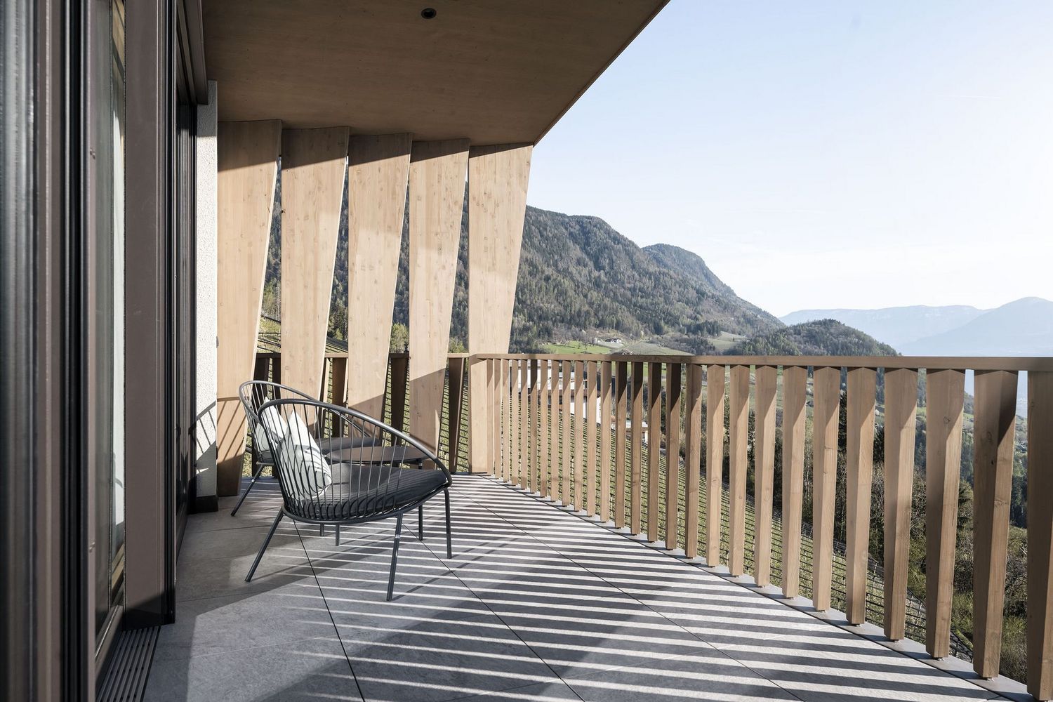 Moderner Balkon mit zwei Stühlen und Holzgitter mit Blick auf bewaldete Berge.