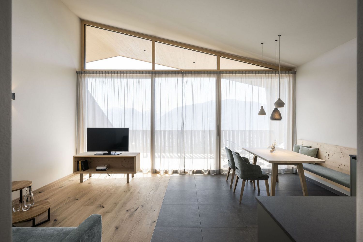 Helles, modernes Wohnzimmer mit großem Fenster, Fernseher auf Holzschrank, Esstisch mit Stühlen und Bank, minimalistischer Stil