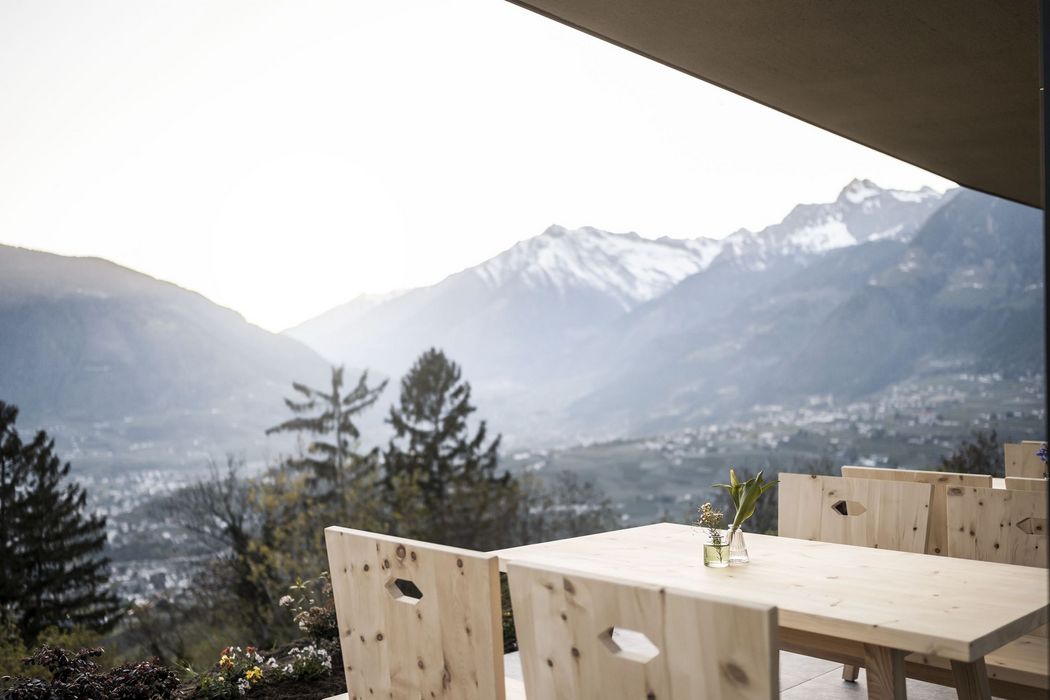 Holztische und Stühle auf einer Terrasse mit Blick auf schneebedeckte Berge und ein Tal im Hintergrund