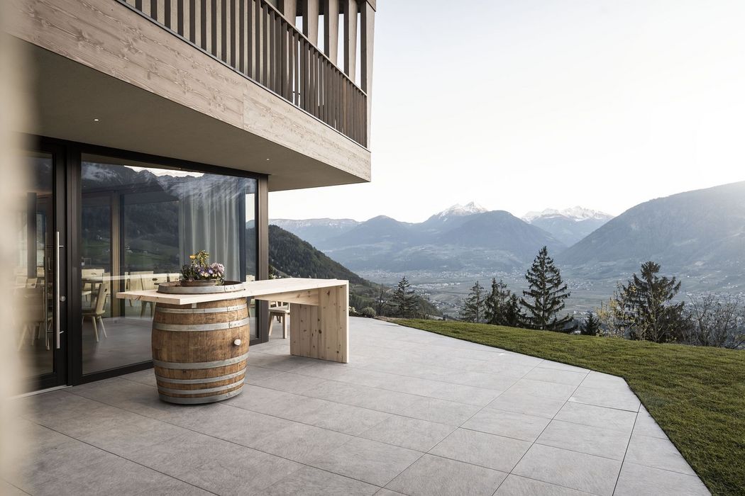 Terrasse mit Tisch aus Holzfass vor modernem Haus mit Bergpanorama im Hintergrund