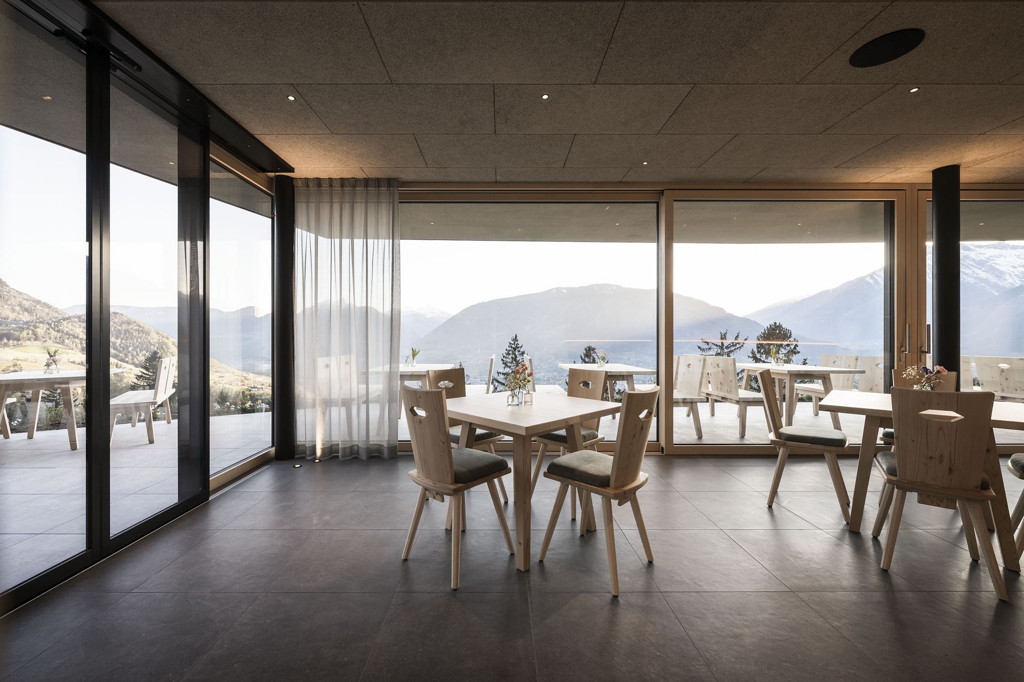 Modernes Restaurant mit Holzstühlen und Tischen, großer Glasfront mit Bergpanorama