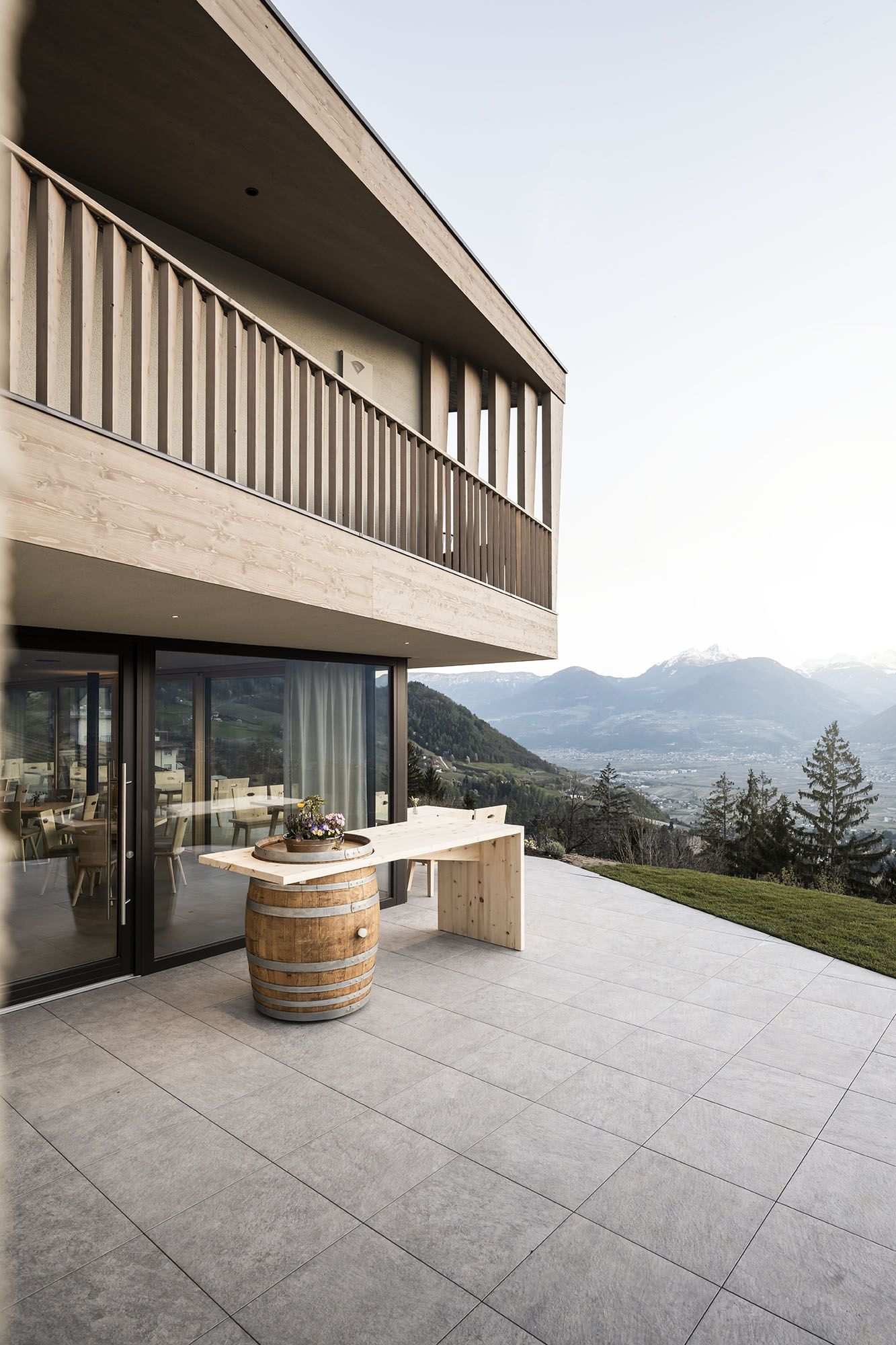 Moderner Holzbau mit Balkon, Terrasse mit Fass und Holztisch, Blick auf Berge und Tal