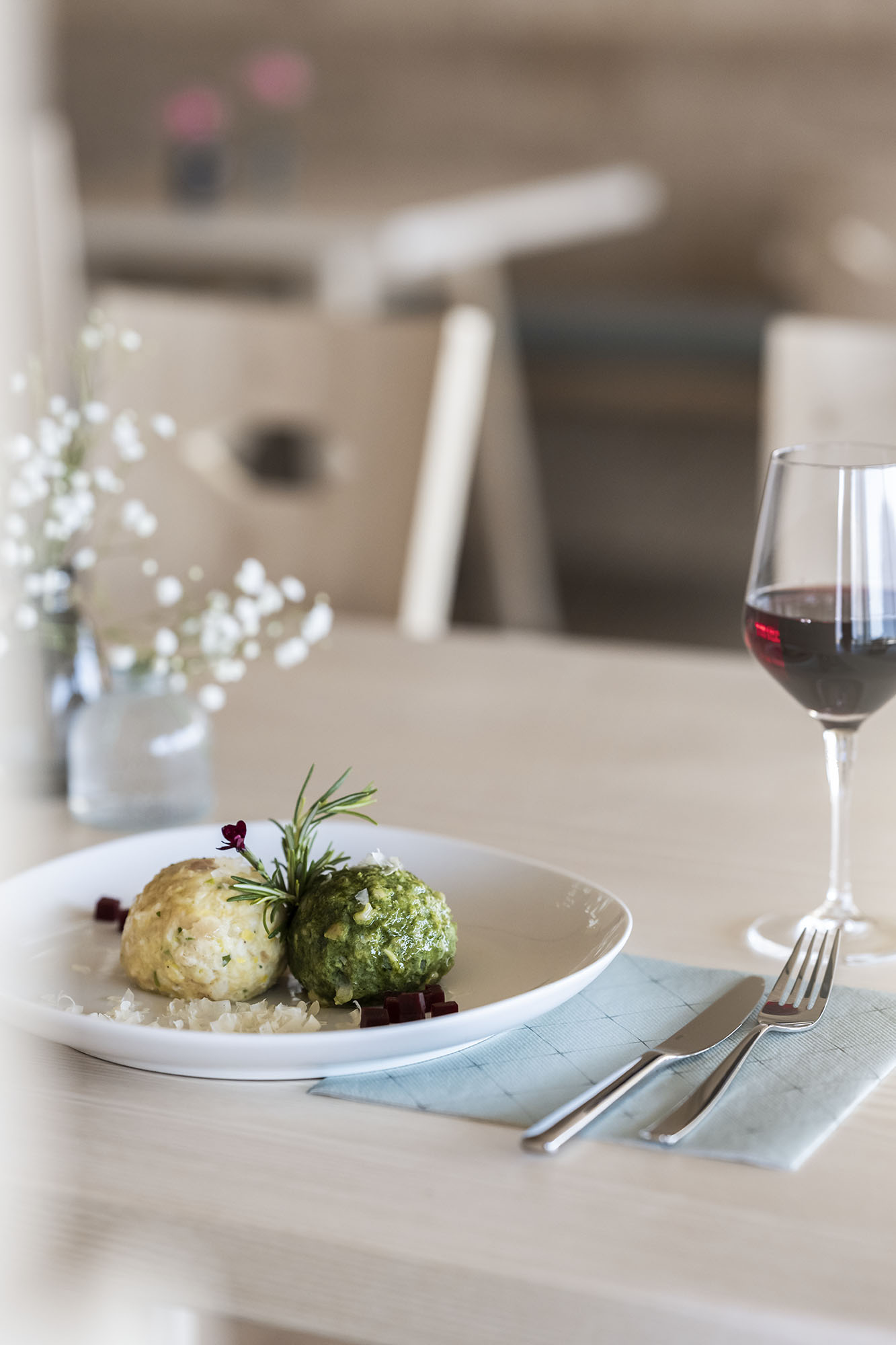 Teller mit zwei Knödeln, ein Glas Rotwein, Besteck auf einem hellen Holztisch