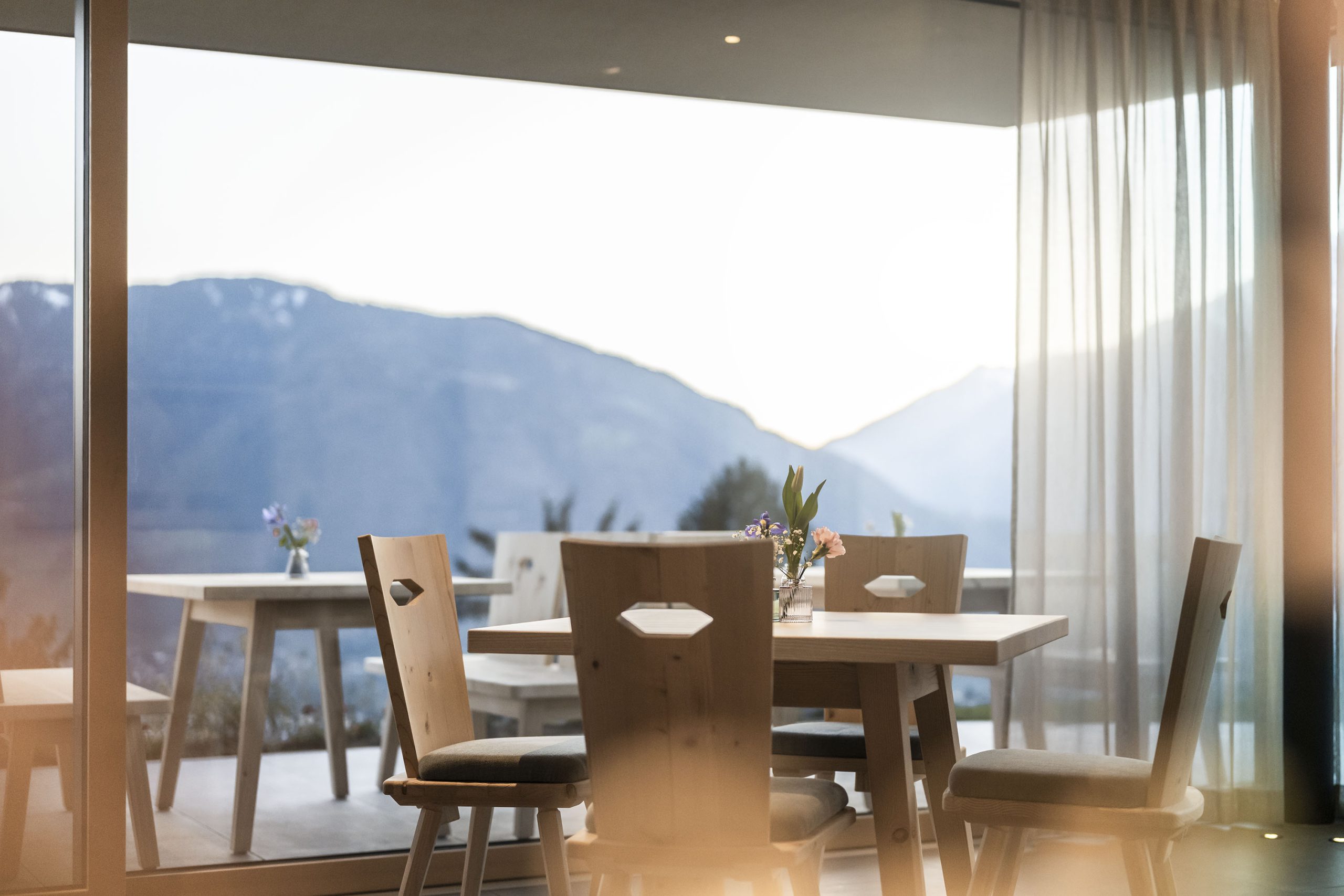 Holztisch mit Stühlen und Blumenvase in hellem Raum mit Panoramablick auf Berge
